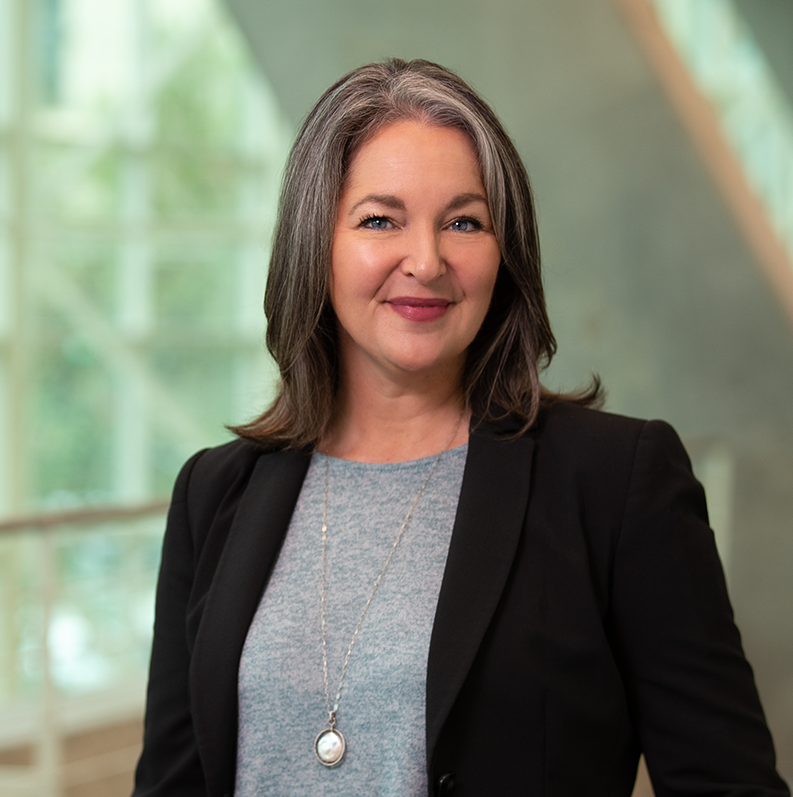 melanie huggins is a person with black hair with gray streaks wearing a gray shirt and black jacket