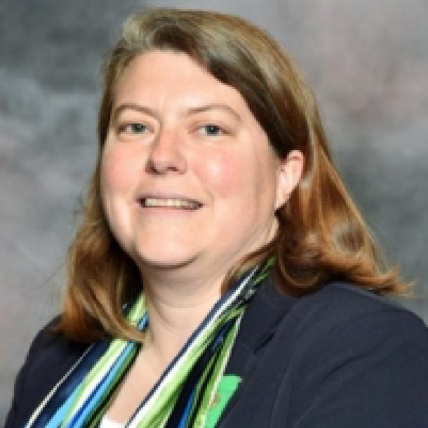 lynn is a person with medium length light brown hair wearing a multi-colored girl scout scarf and navy blue jacket