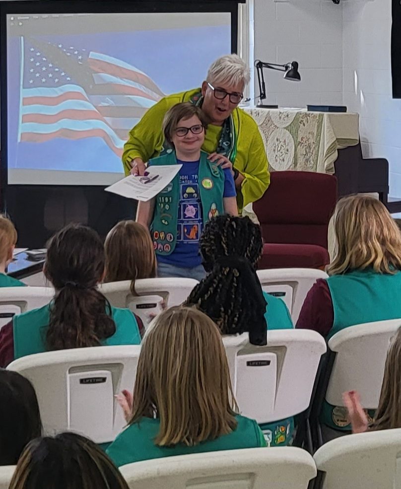 former CEO Lora Tucker stands with Girl Scout Amelia in front of Amelia's troop friends