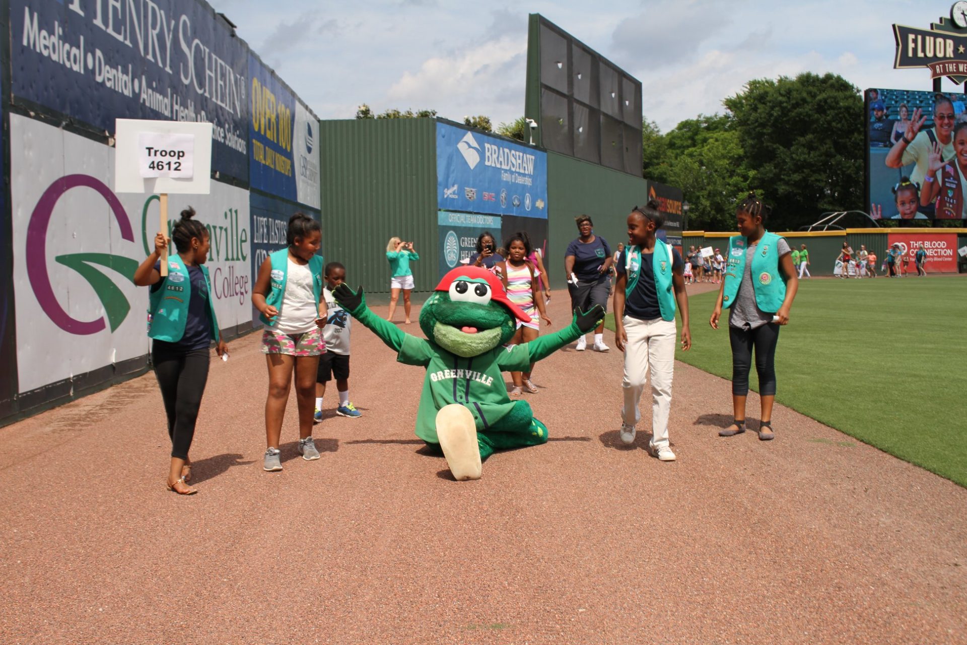  A group of Girl Scouts in uniform smile at Greenville Drive mascot doing a split on the field during Girl Scout Day at the Greenville Drive. 