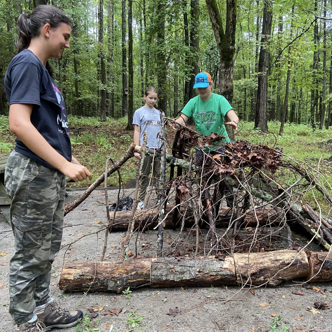 three girl scouts make a shelter out of sticks