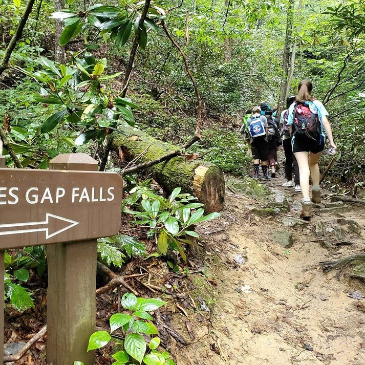 girl scouts hike on a trail that has a sign saying "Jones Gap Falls"