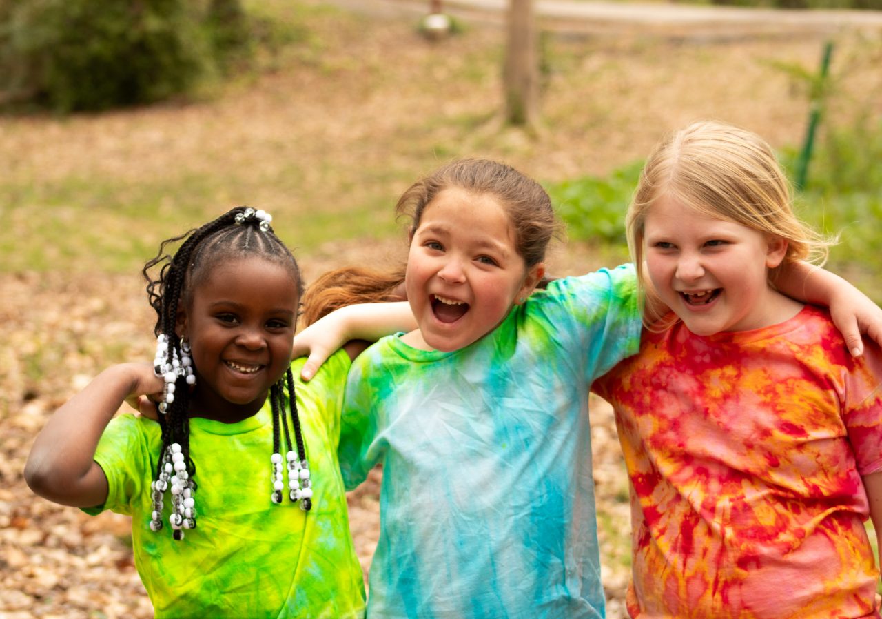 Three campers in tie-dye shirts laugh together at Camp Mary Elizabeth