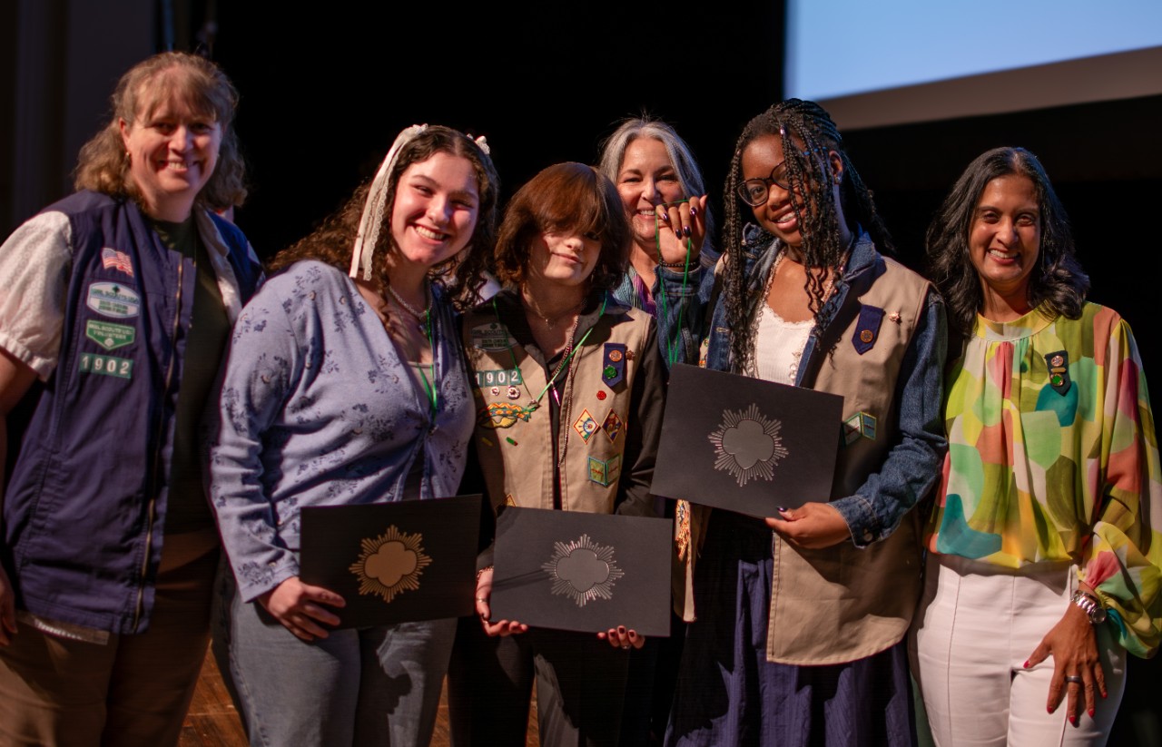 three Silver Award Girl Scouts pose with troop leader and council representatives at ceremony