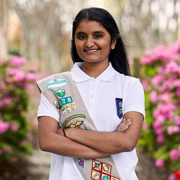 a Girl Scout with a tan sash smiles at the camera