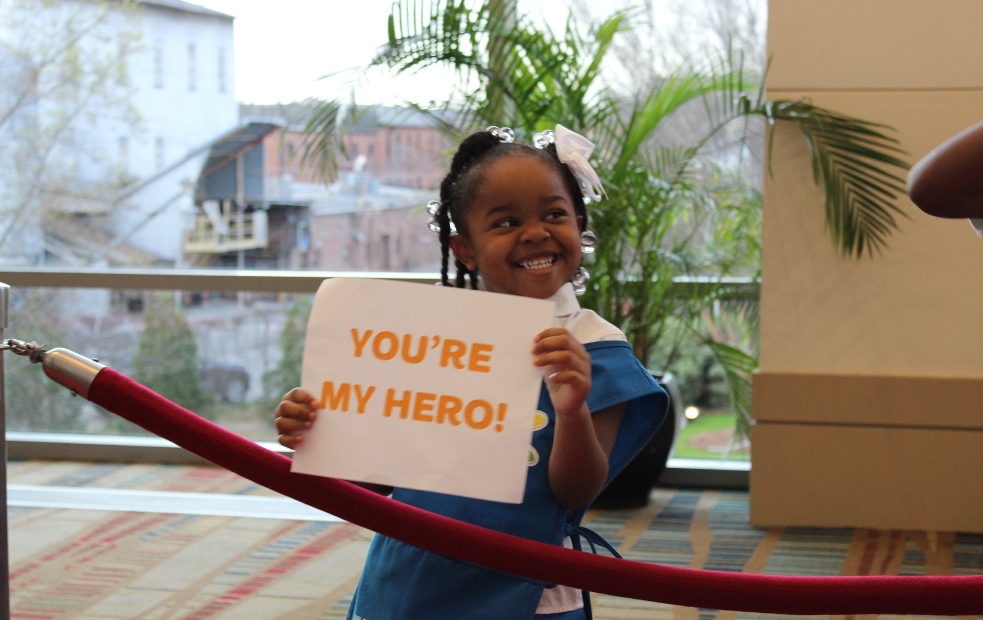  A Girl Scout Daisy holds up a sign that reads "You're my hero!" in orange text 