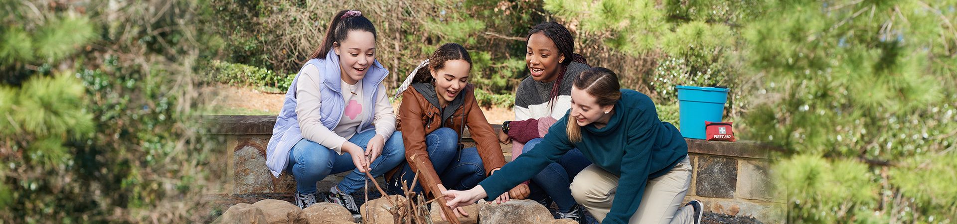  Four older girl scouts dressed in cold-weather outdoor clothes make a fire together. 